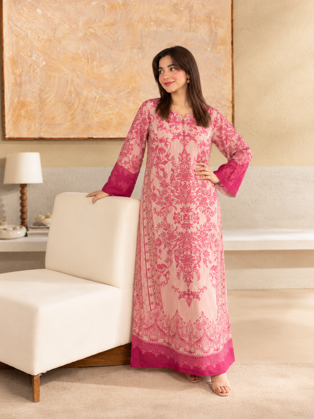 Gulbahar Kaftan pink crepe outfit, standing beside the cream lounge chair.